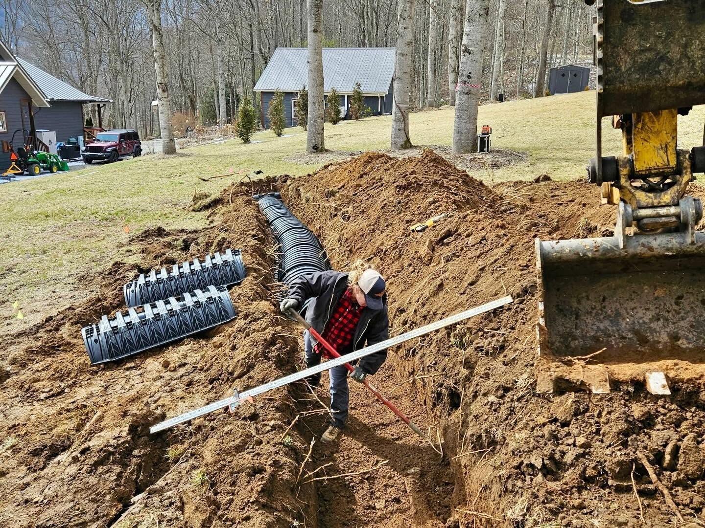 Worker beside large excavator digging a trench in a muddy yard