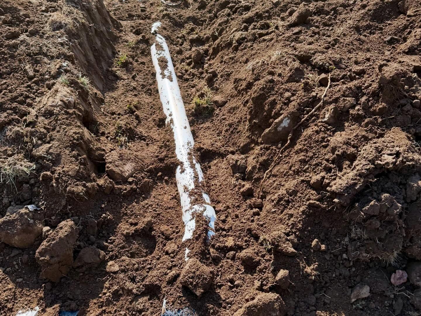 Broken white pipe exposed in dirt trench
