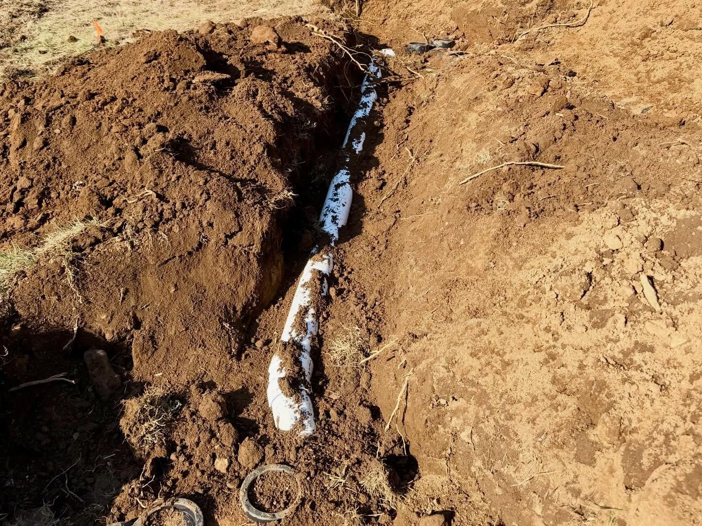 A narrow trench in dry soil with a white pipe or cable running through it