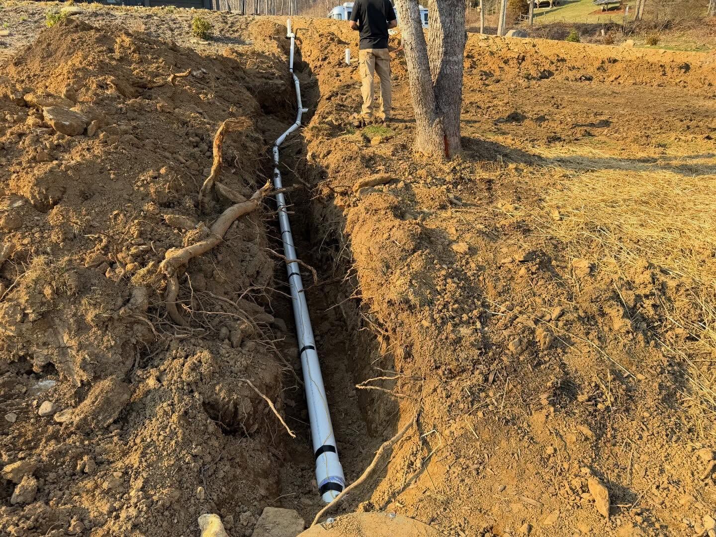 White pipe laid in a dirt trench on a hillside, with workers near the top of the slope