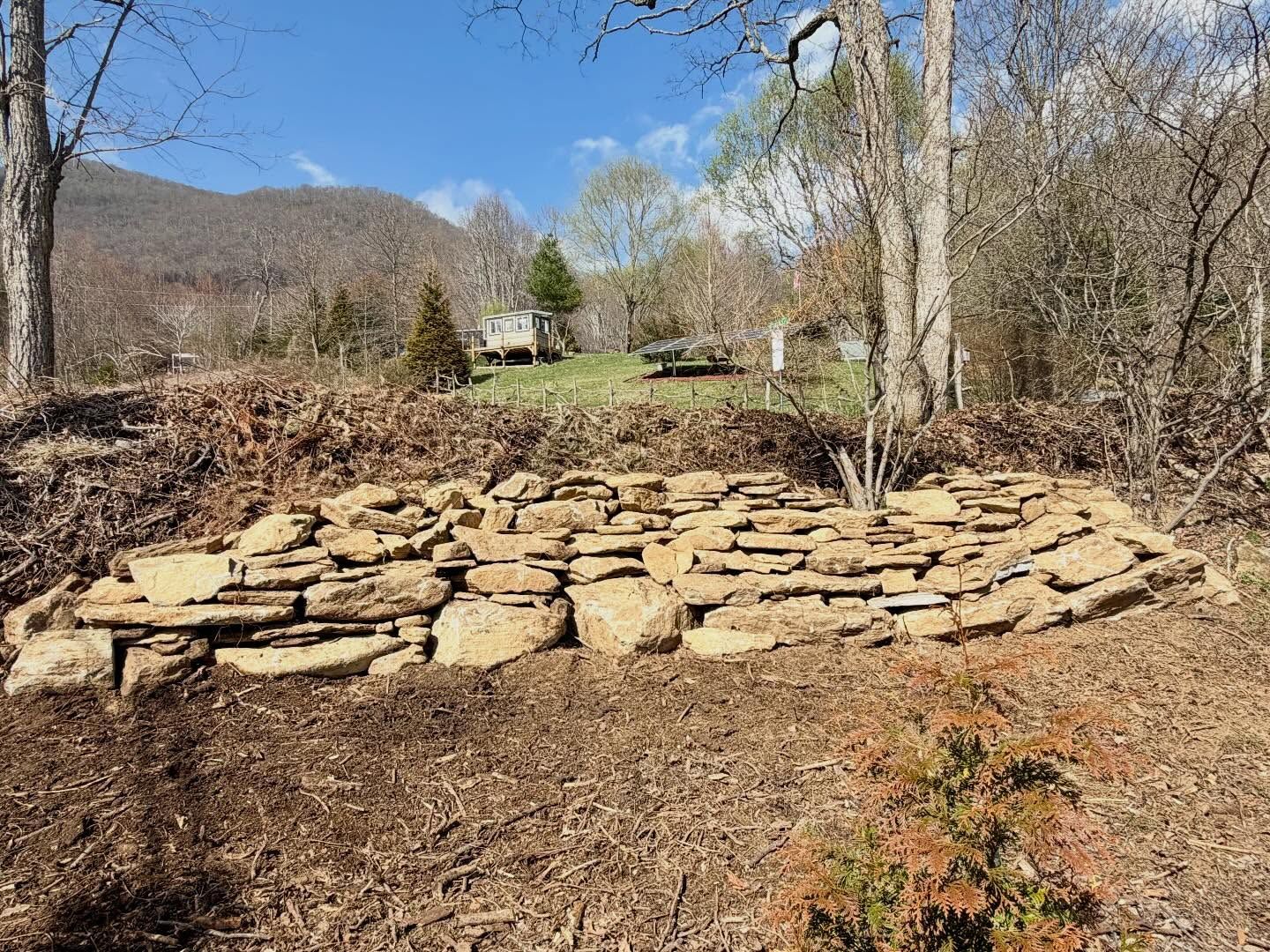 Stone terraced garden bed in a wooded yard with mountains and a blue sky in the background