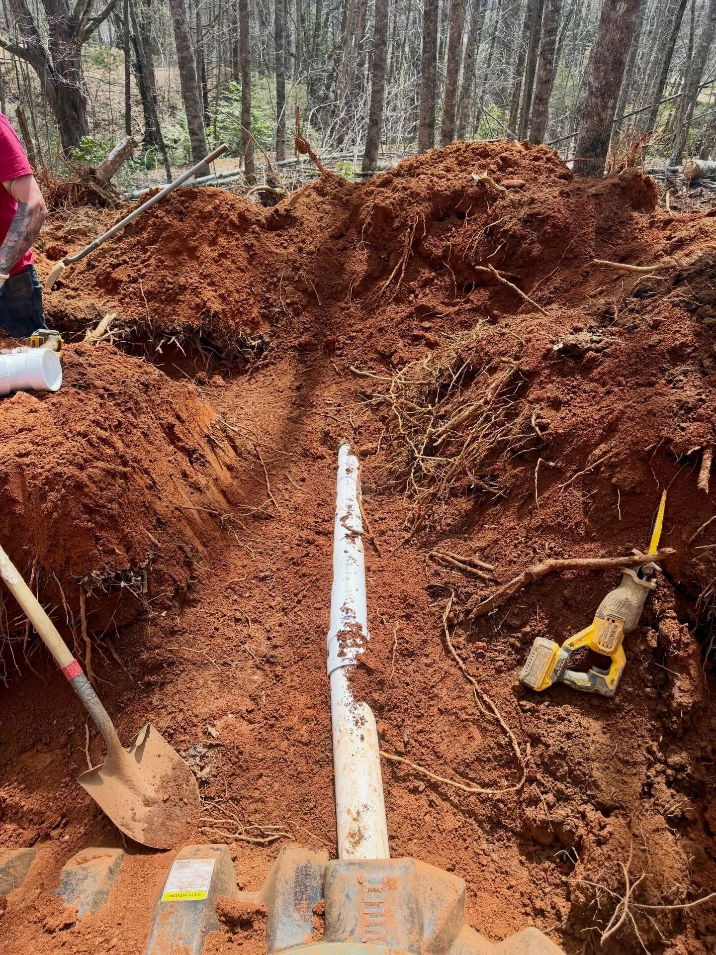 Trench excavation with shovel, pipe, and digging tools in a wooded area