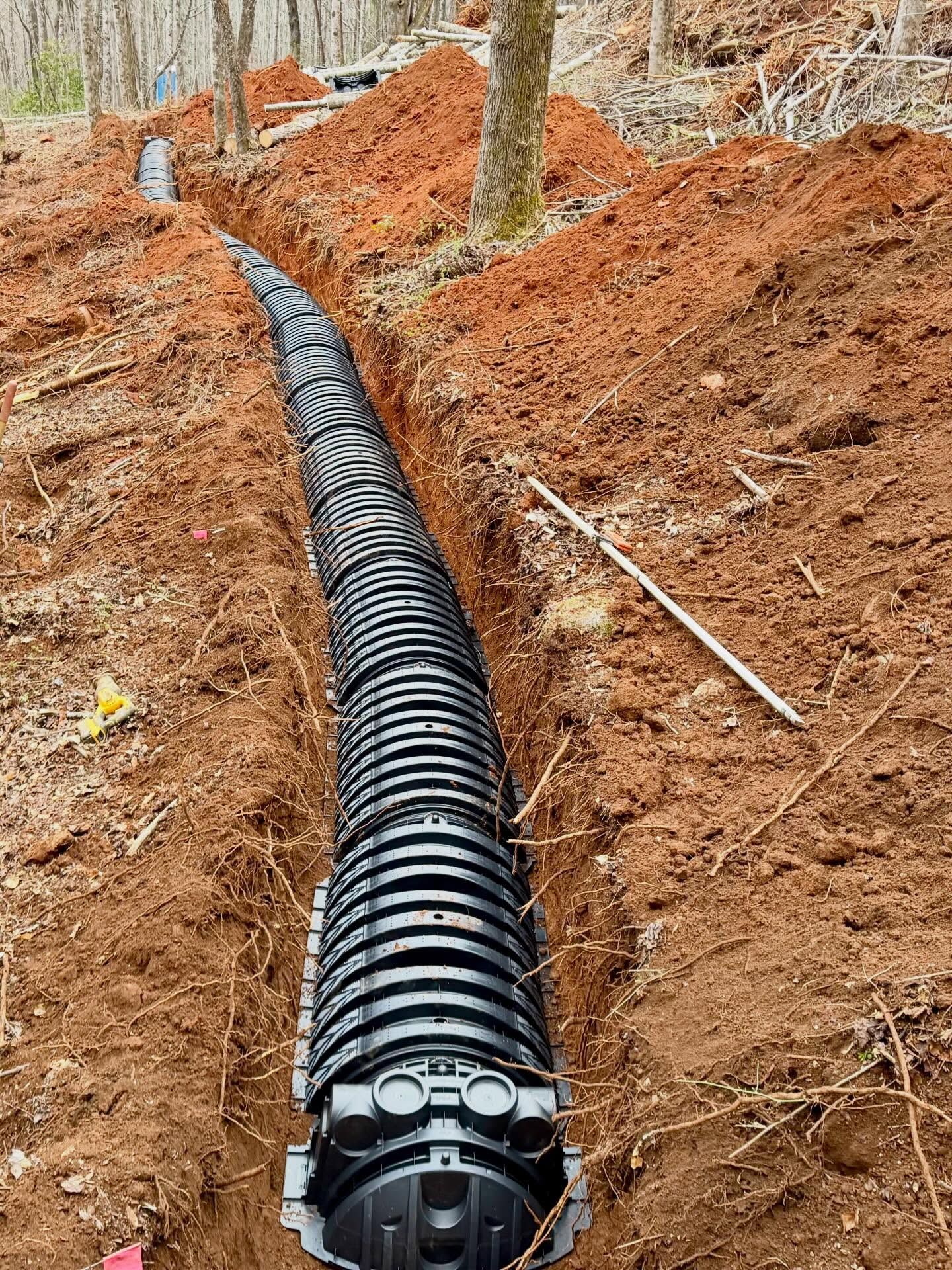 Black corrugated pipe laid in a muddy trench through a wooded area