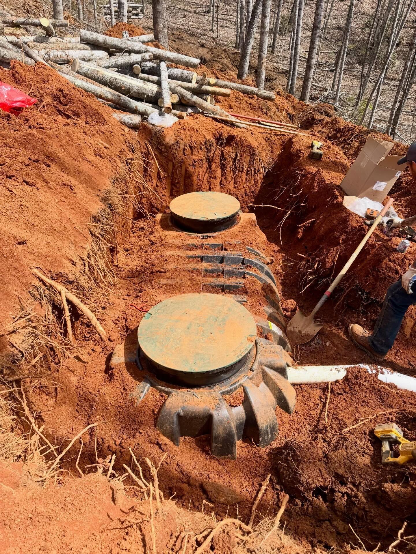 Excavation site with two large round concrete tanks in a red dirt trench, surrounded by logs and tools