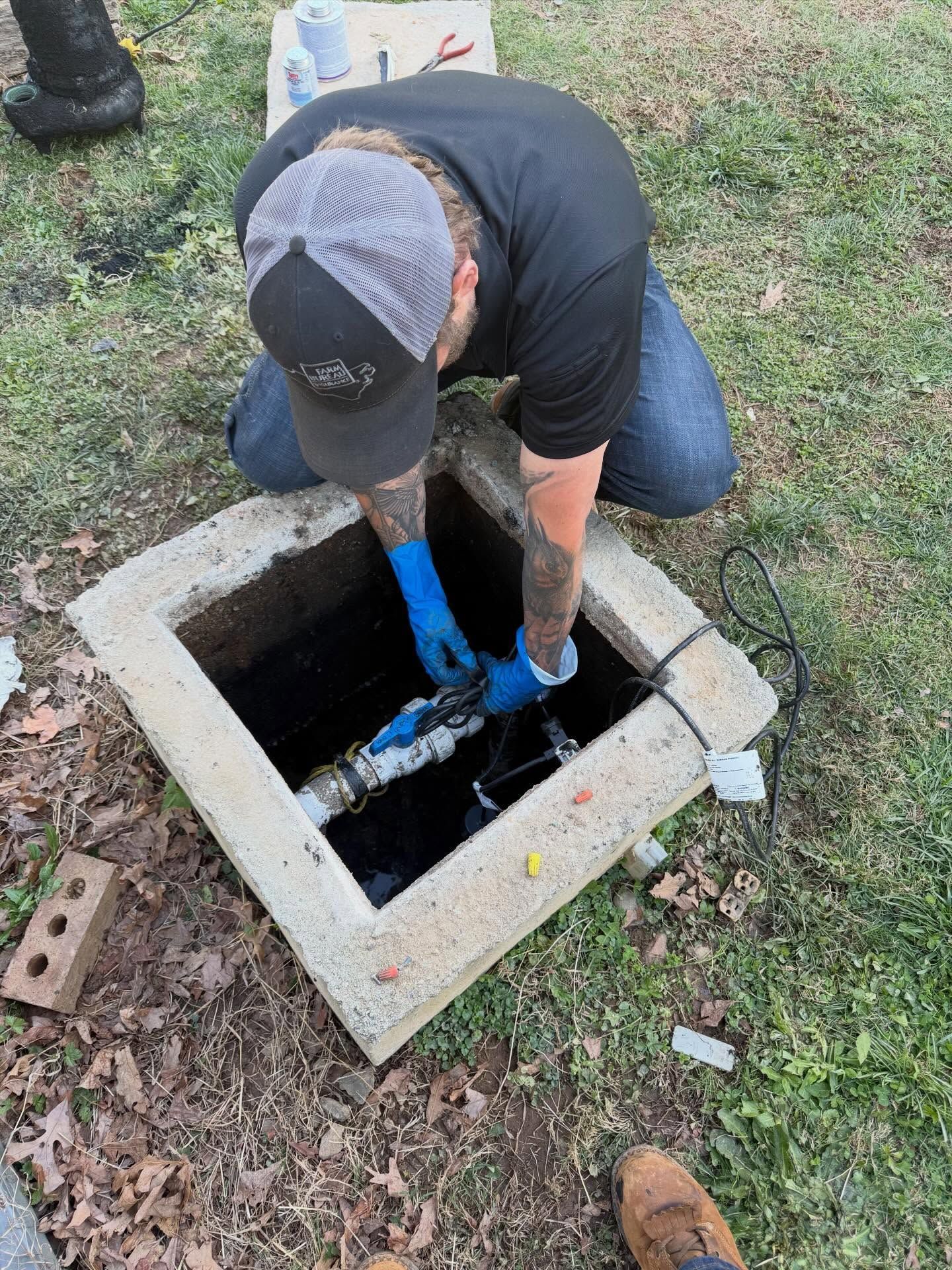 Worker in blue gloves inspecting an open utility box in the ground outdoors.