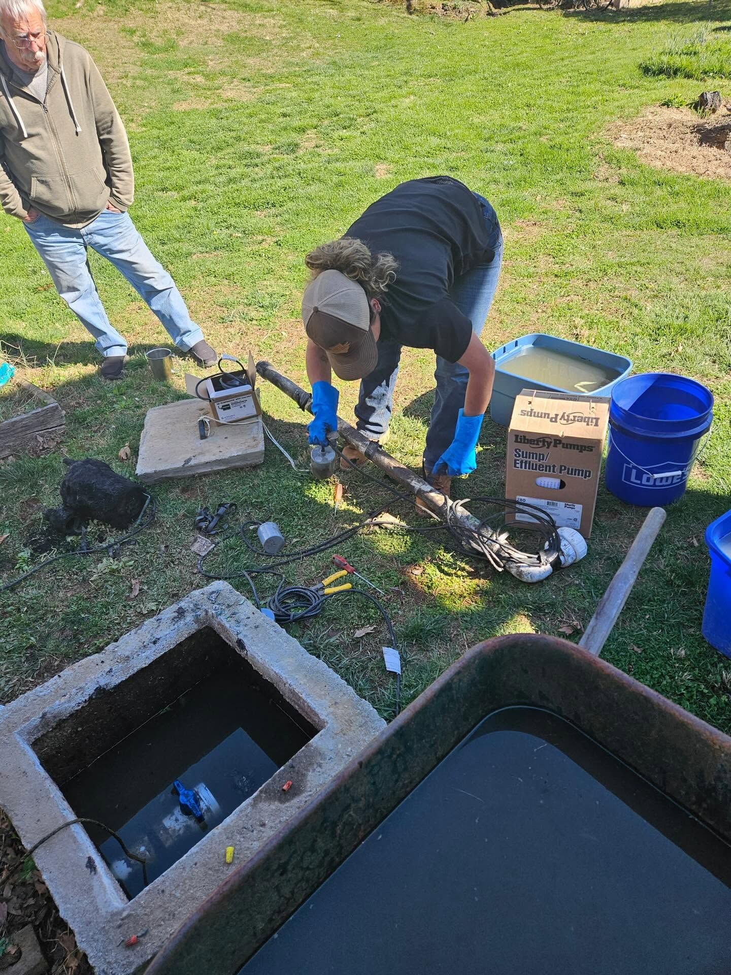 People setting up tools and containers beside a backyard fire pit on grass