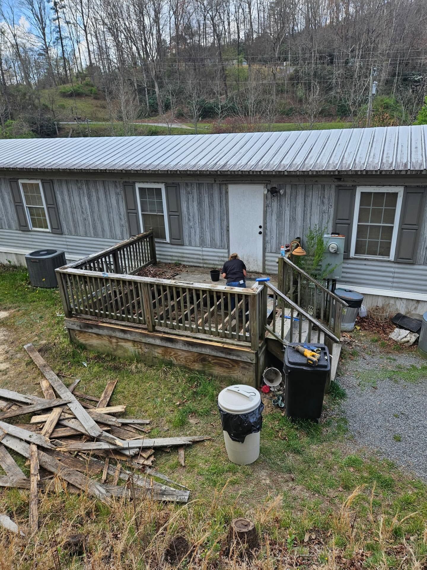 Person on wooden porch with railings and potted plants outside a gray house