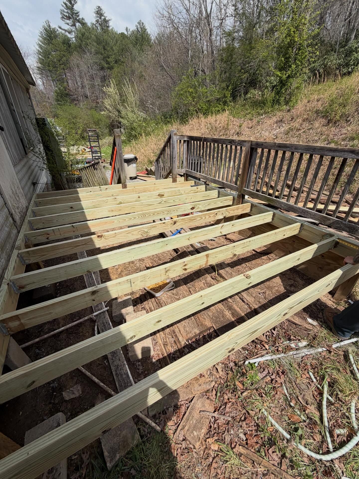 Partially built wooden deck stairs beside a house, with exposed joists and railing on a wooded hillside