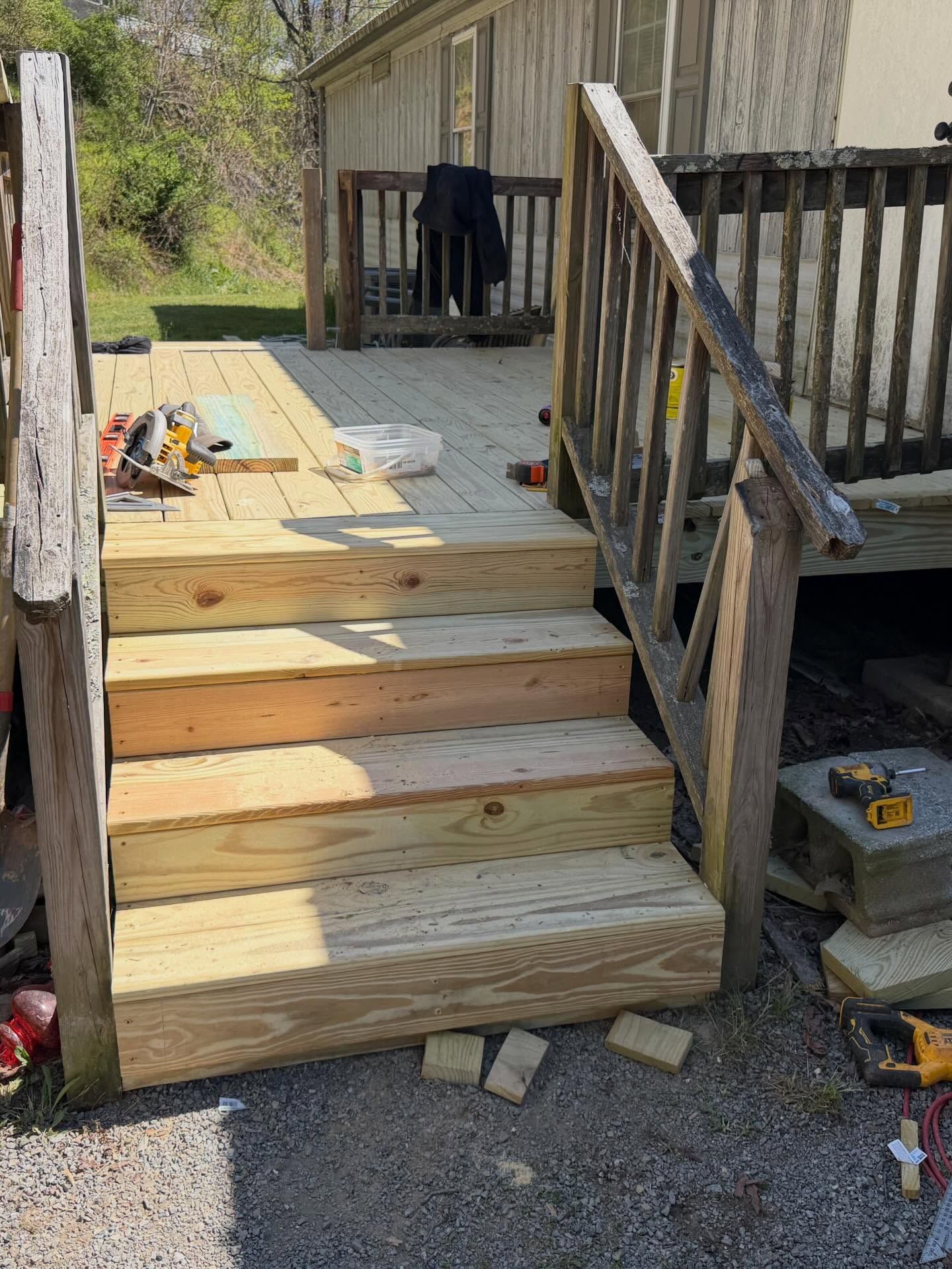Wooden steps leading to a deck beside a weathered house, with tools and construction materials nearby.