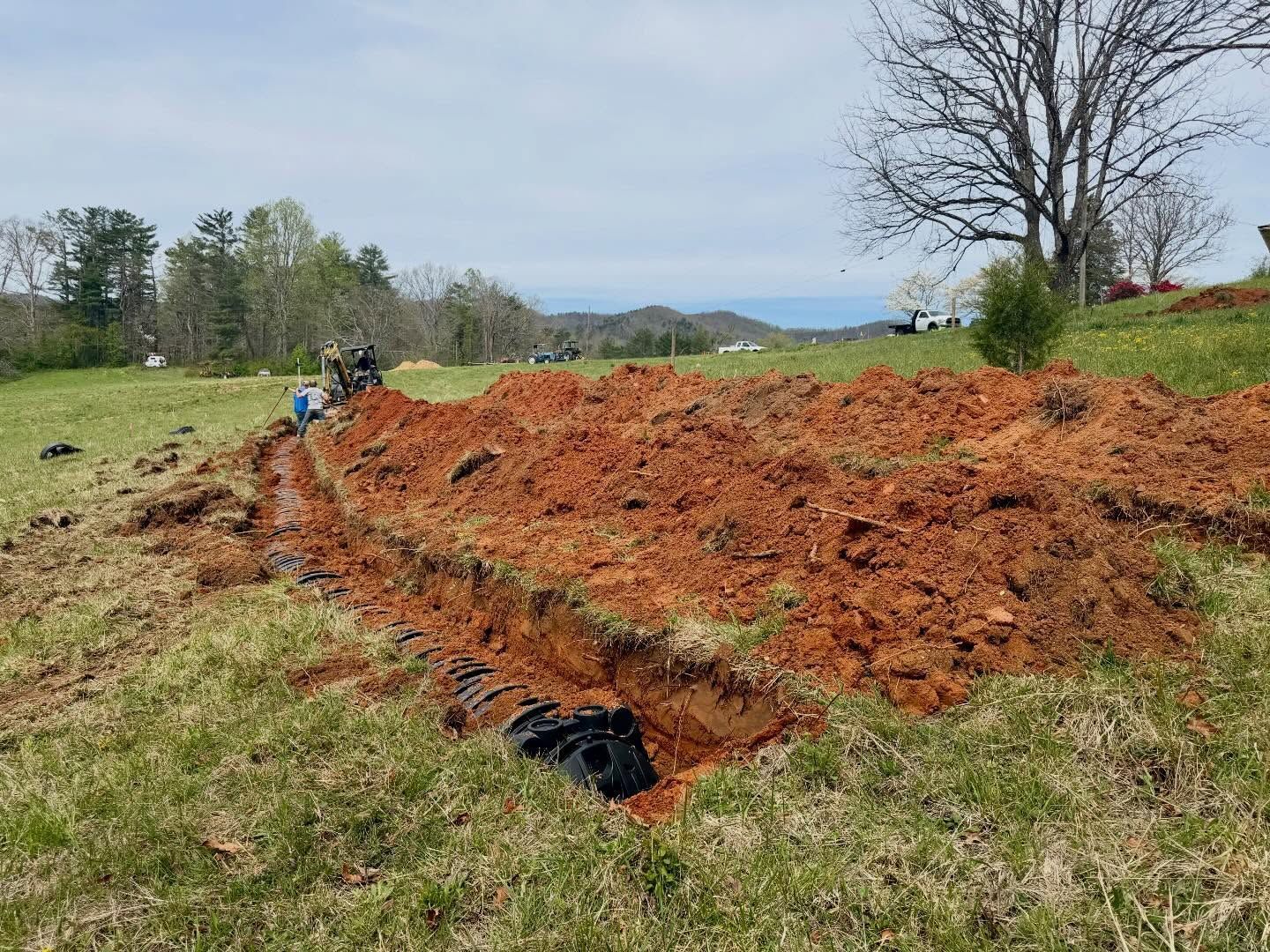 Large pile of red dirt in a grassy field with a blue tarp and trees in the background