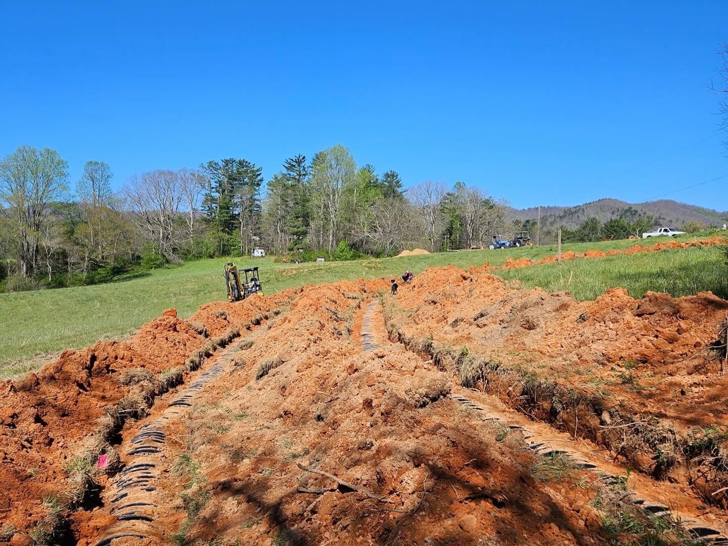 Rutted orange dirt field under a clear blue sky, with trees and hills in the distance.