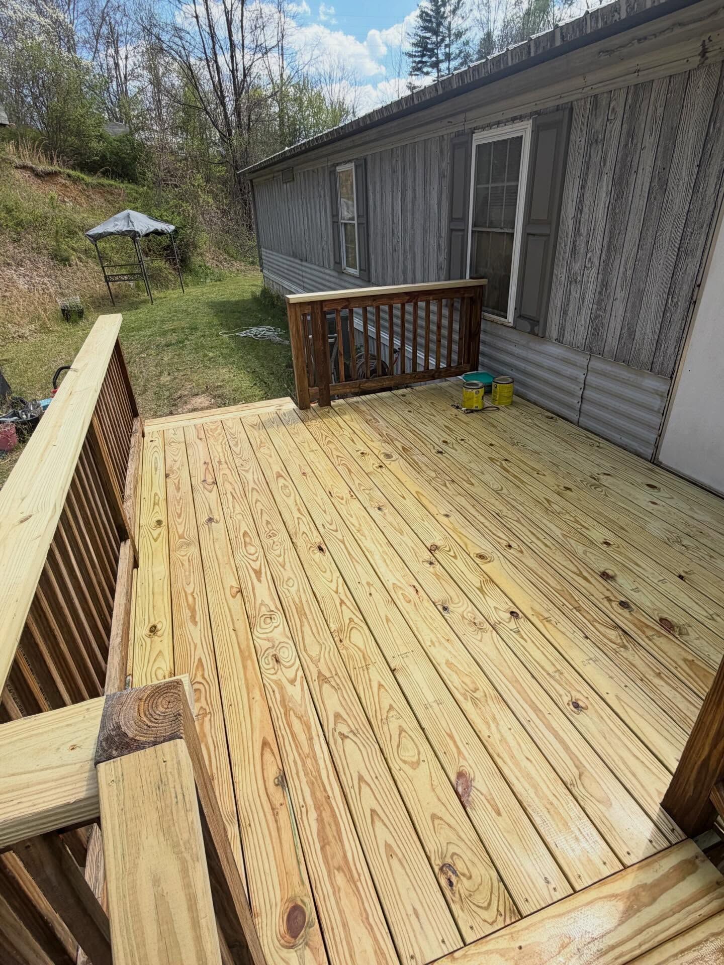 Wooden deck with railing beside a gray house, overlooking a grassy yard with a patio umbrella.
