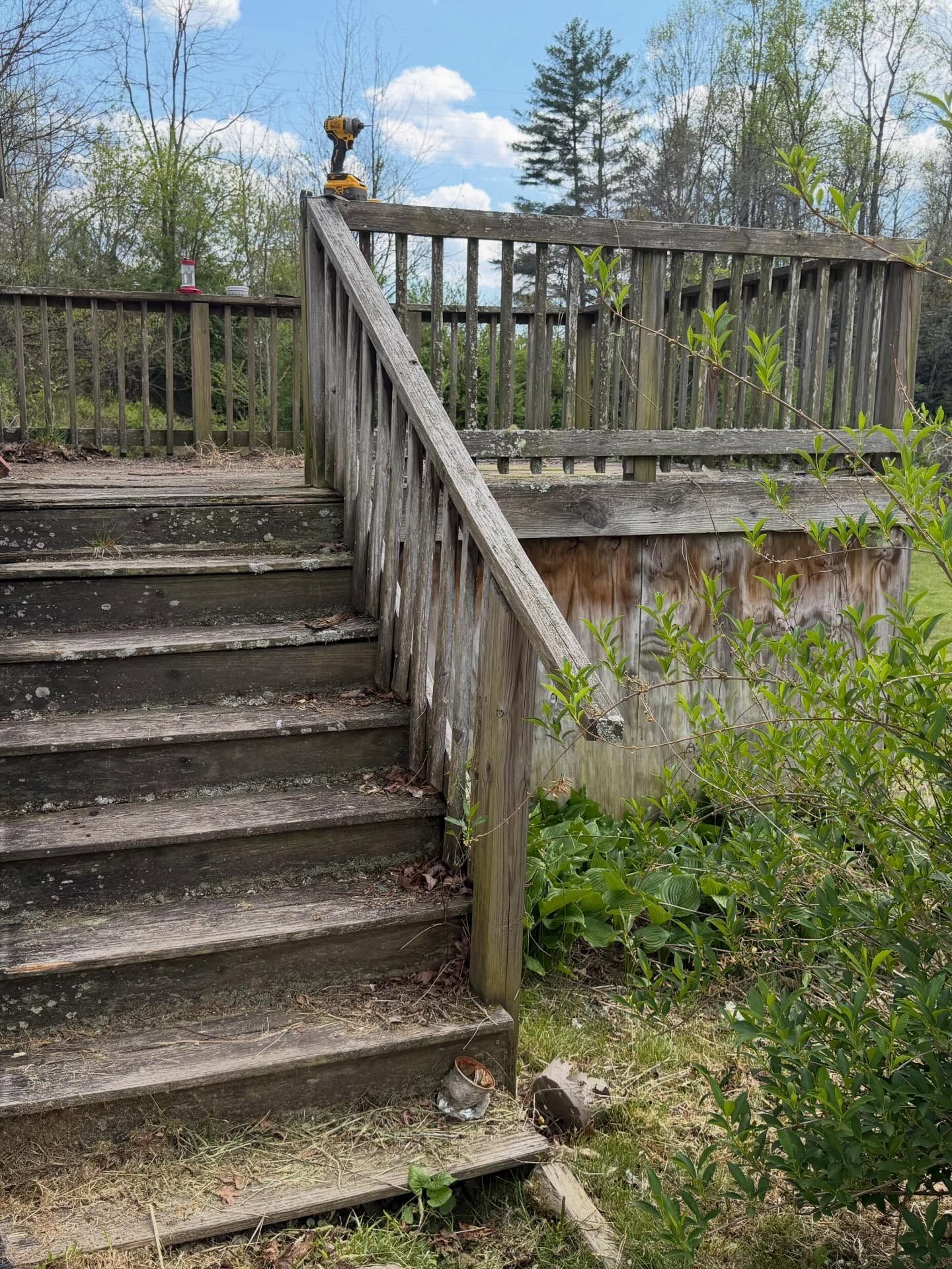 Weathered wooden stairs leading to a deck railing beside a grassy slope under a partly cloudy sky
