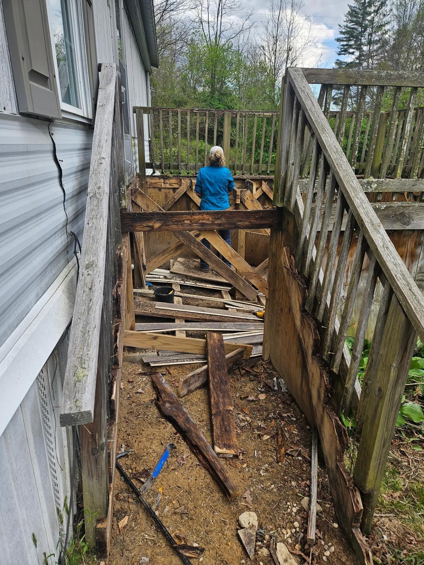 Worker in blue shirt inspecting debris-filled trench beside house and stairway.
