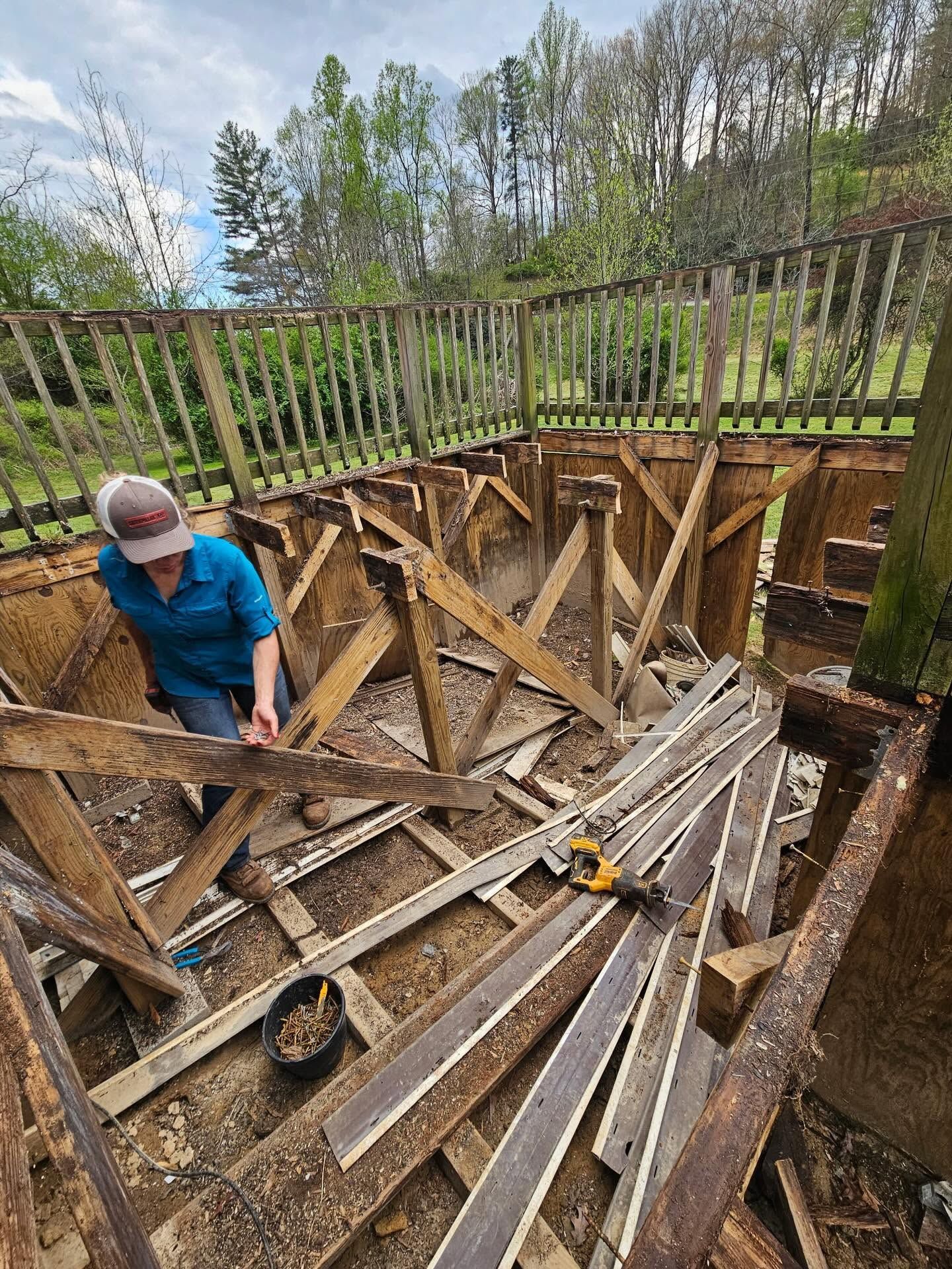 Worker inside a large wooden pit with slanted supports, outdoors under a fenced deck.