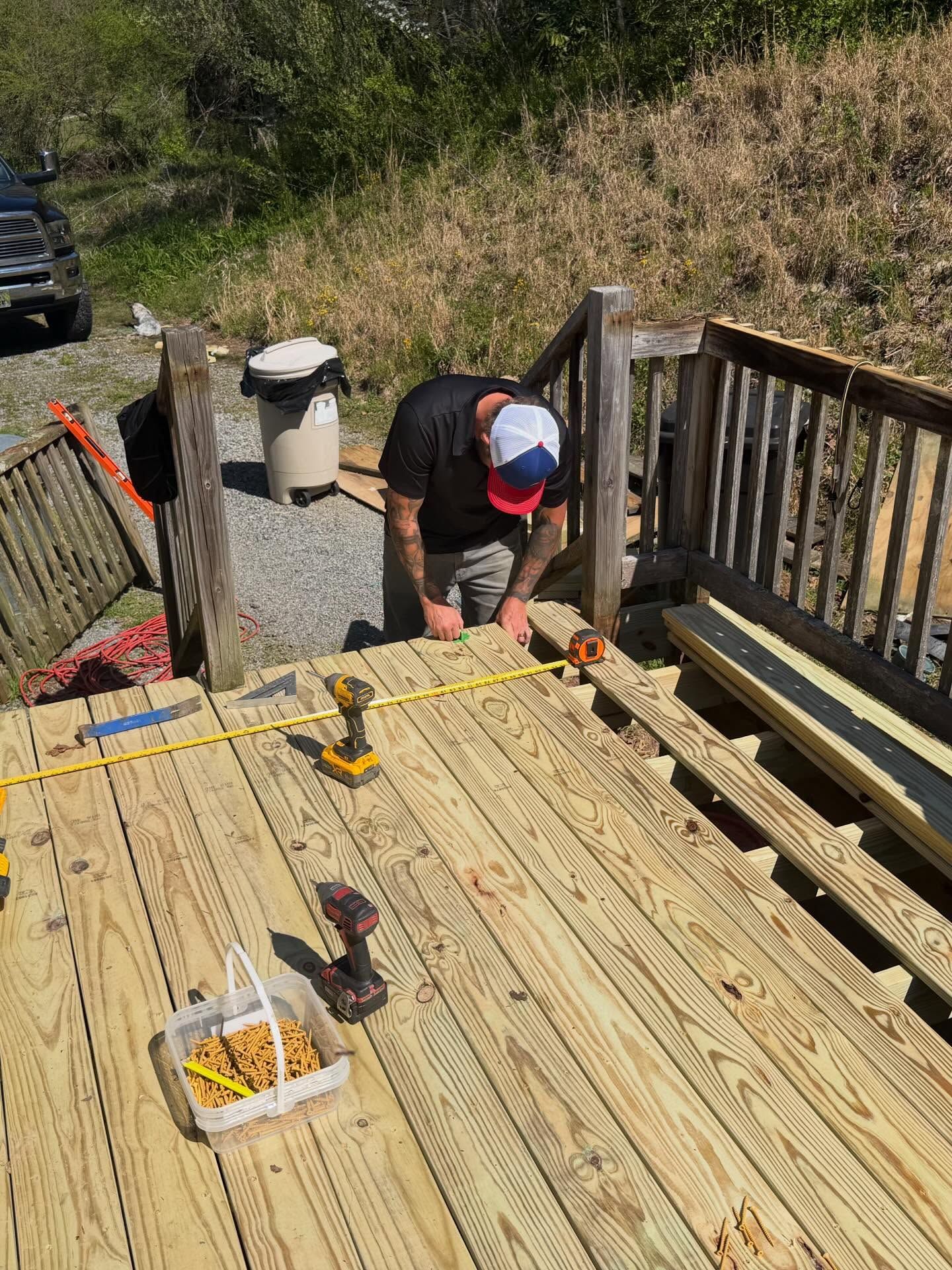 Person kneeling on a wooden deck, using a tape measure while building or repairing it.