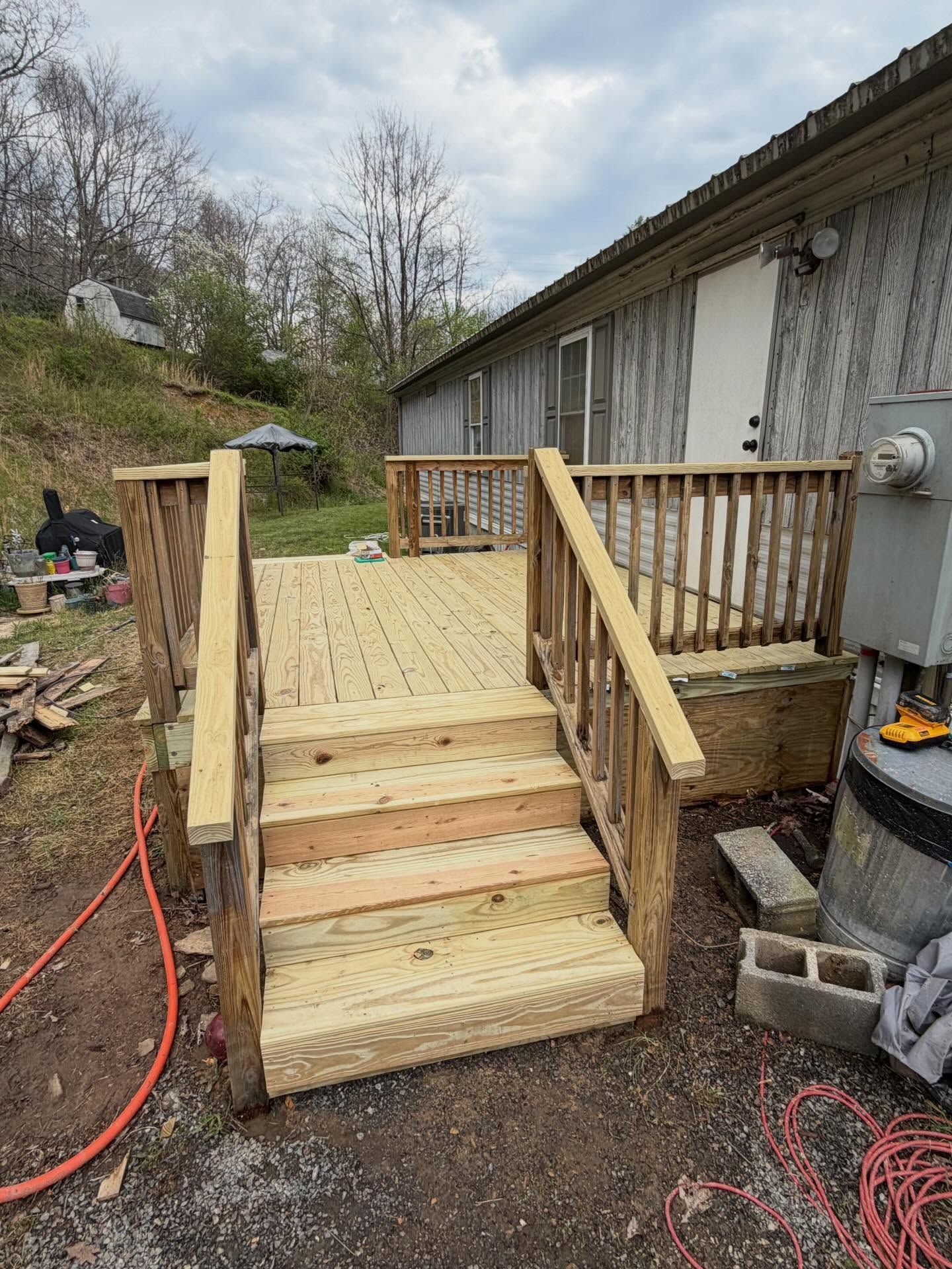 New wooden wheelchair ramp and steps beside a gray building on a dirt driveway