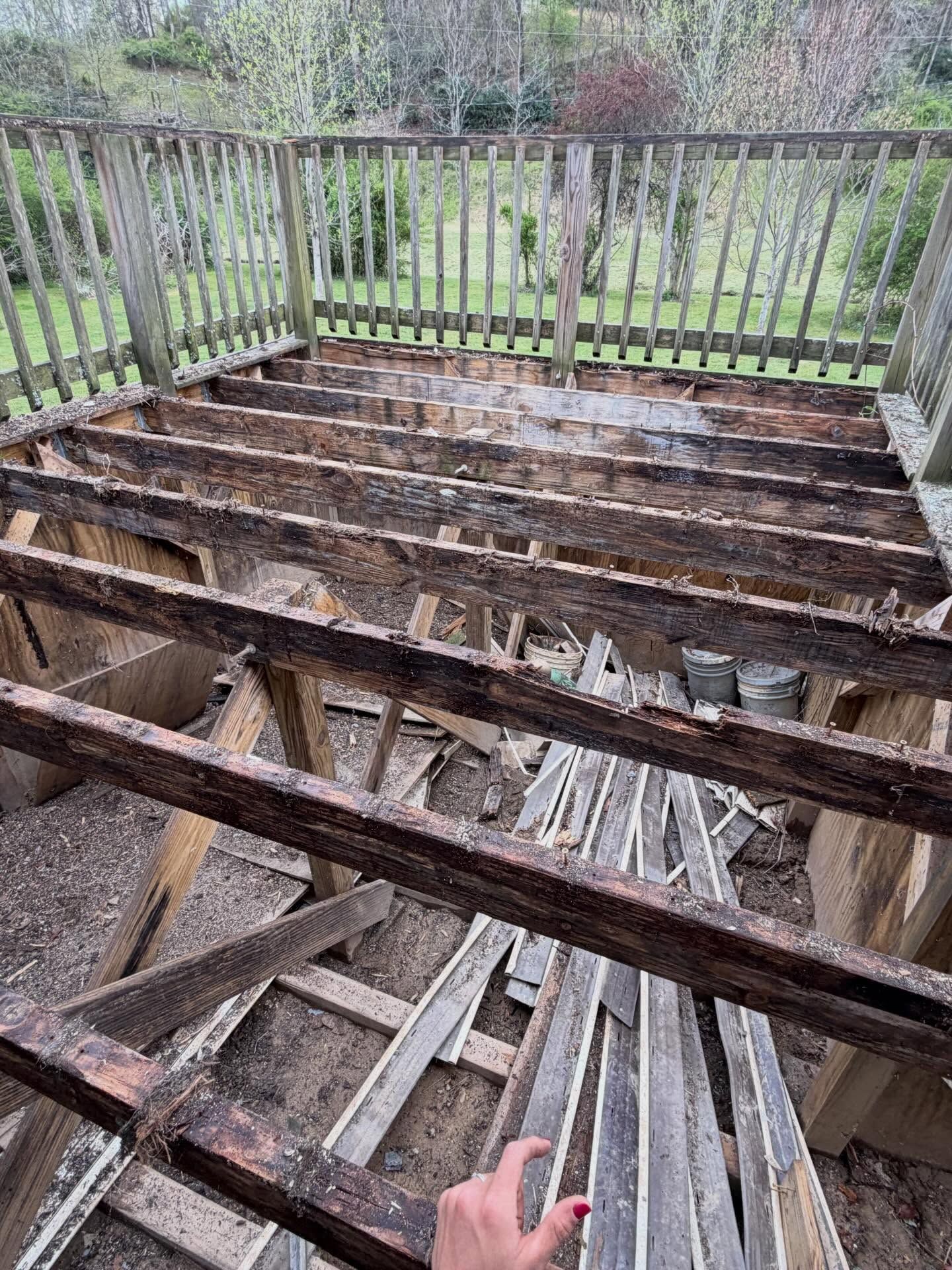 Partially demolished wooden deck with exposed joists and railings overlooking a yard