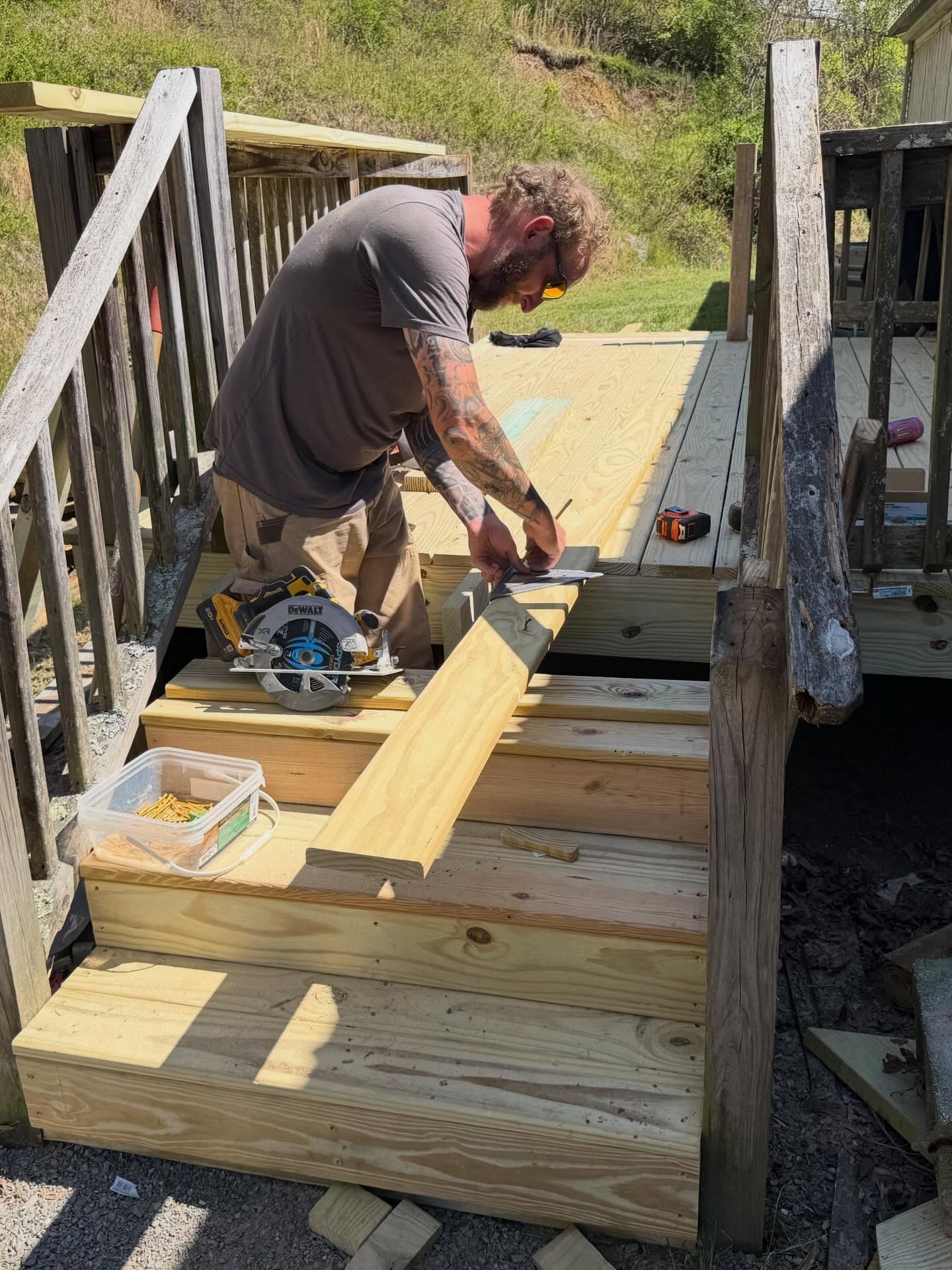 Person cutting wood on a deck with a circular saw, building steps outdoors.