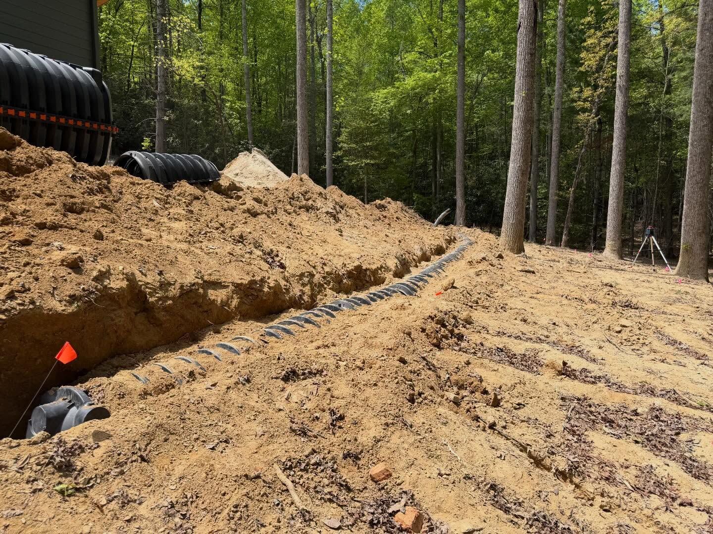 Construction trench with black pipes and a dirt embankment in a forested area
