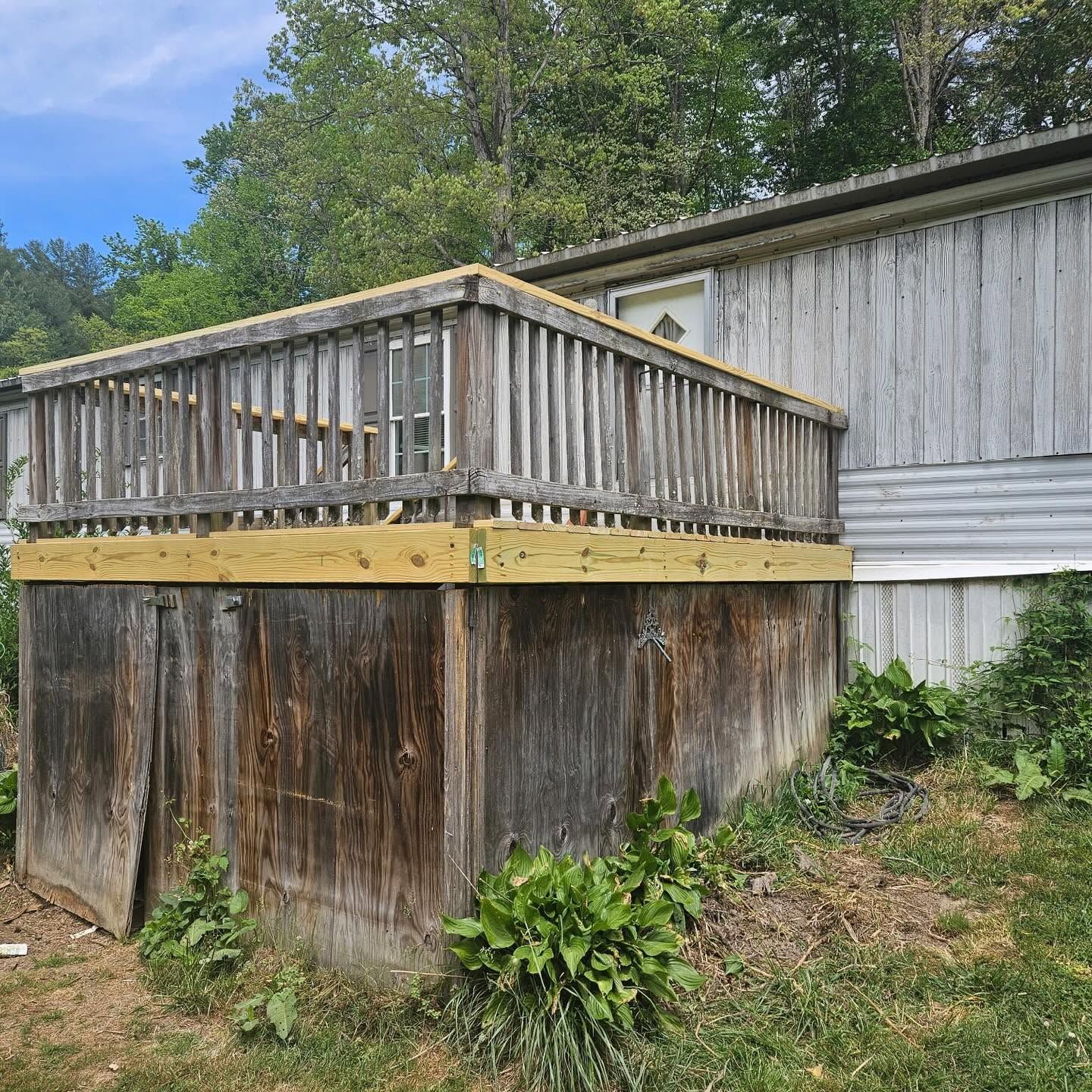 Weathered wooden deck attached to a shed, with a raised platform and railing over a grassy yard.