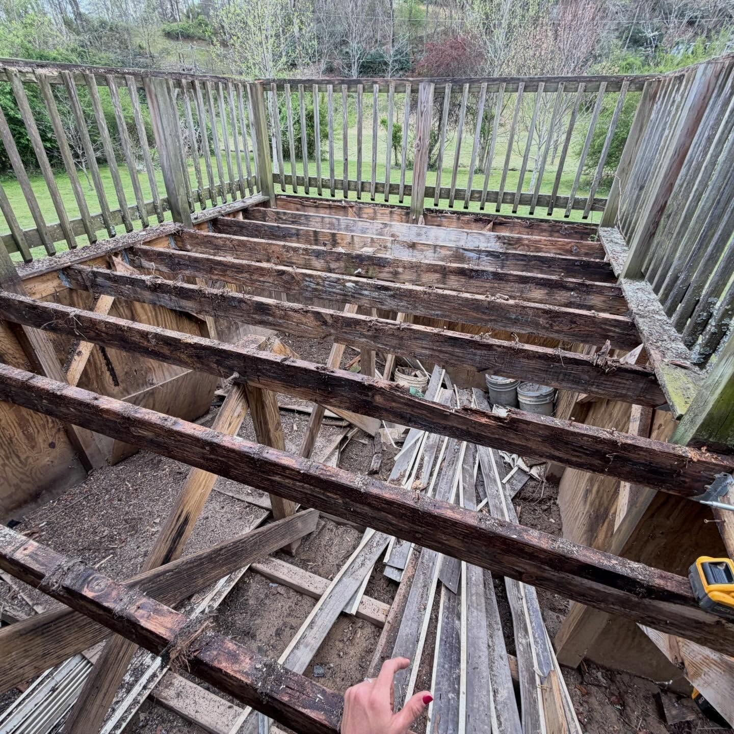 Severely damaged wooden deck with exposed joists and railing, overlooking a backyard.