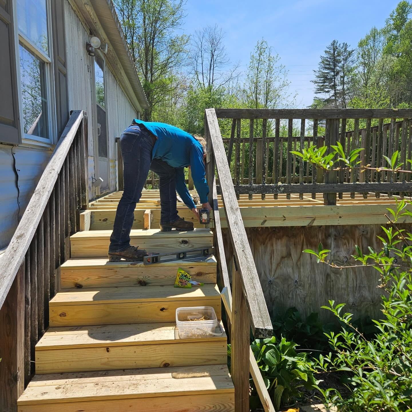 Person bending over on wooden outdoor stairs next to a house, working near a deck in bright sunlight