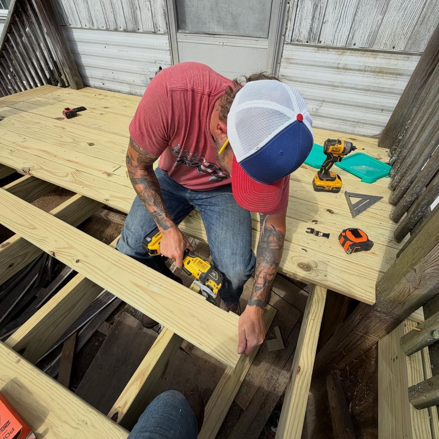 Worker in red shirt installing floor joists on a wooden platform with a power drill