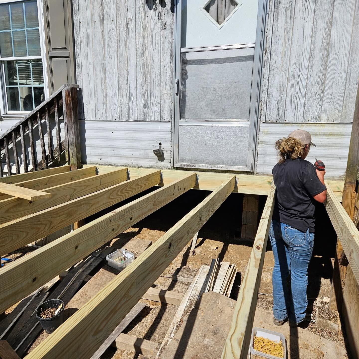 Partially rebuilt wooden deck beside a weathered house, with a person standing on the right.