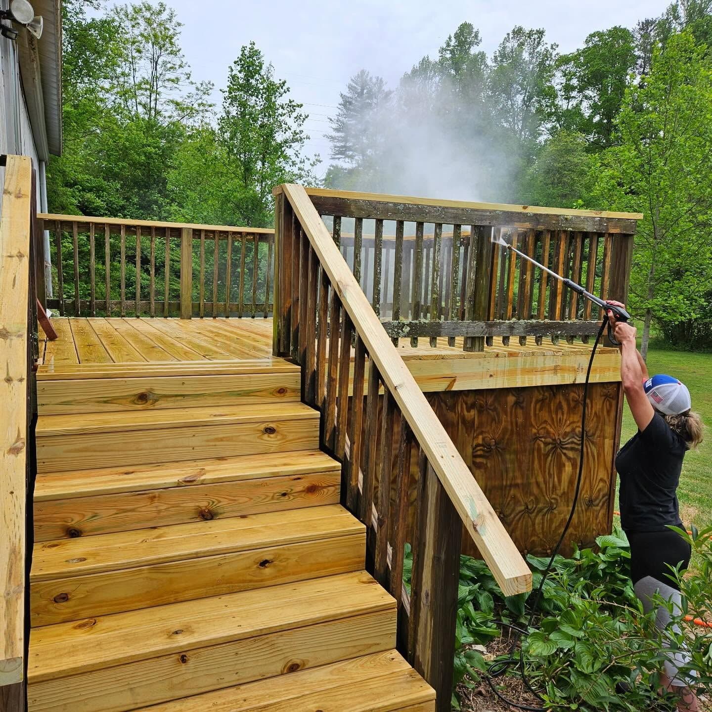Man spraying water near a wet wooden deck and stairs under construction in a leafy backyard