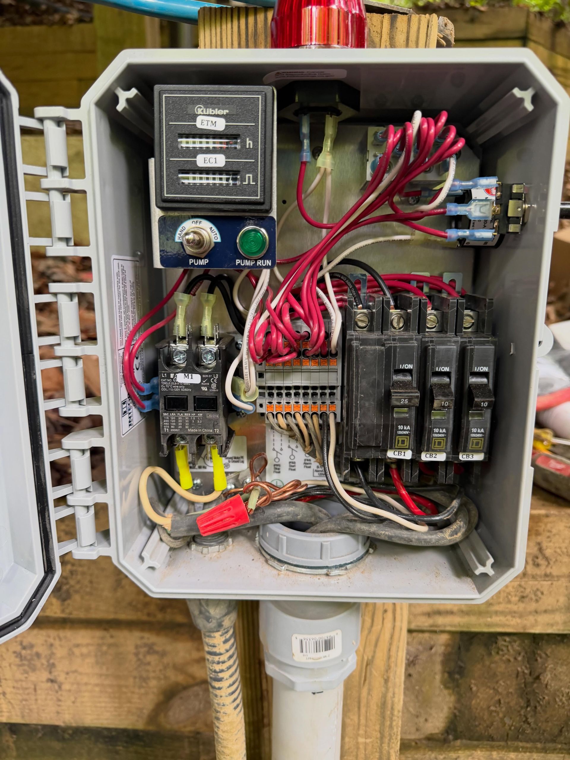 Open electrical control panel with wiring, relays, and switches mounted on a wall post