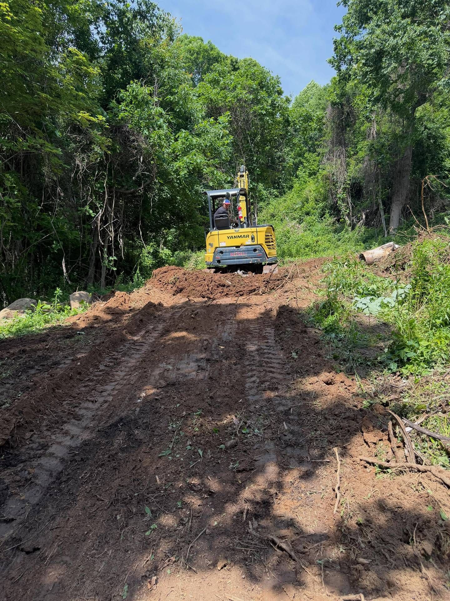 Yellow bulldozer clearing a muddy dirt road through dense green forest