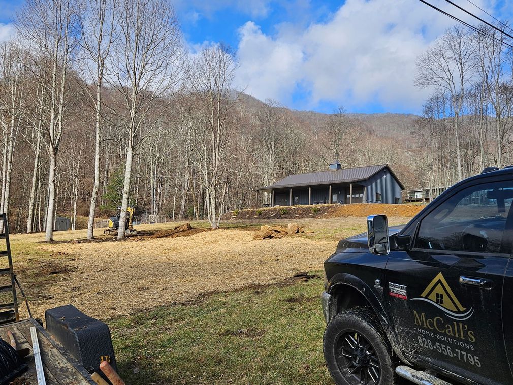 Black off-road truck by a cabin in a leafless wooded clearing under a blue sky