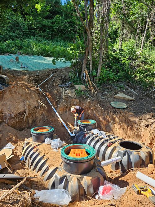 Outdoor mud brick kilns with baskets of orange bricks and a person working among trees in a rural area