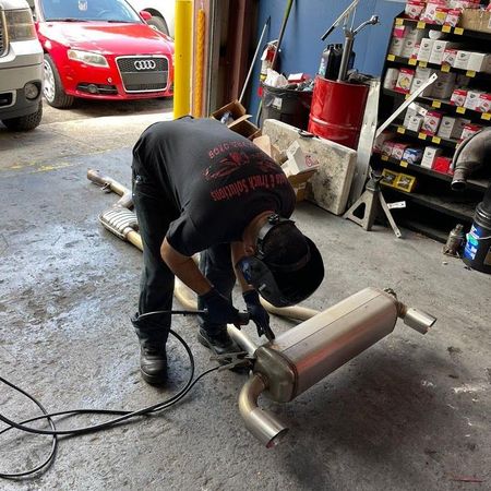Mechanic welding an exhaust pipe in a garage with a red car in the background | Auto & Truck Solutions