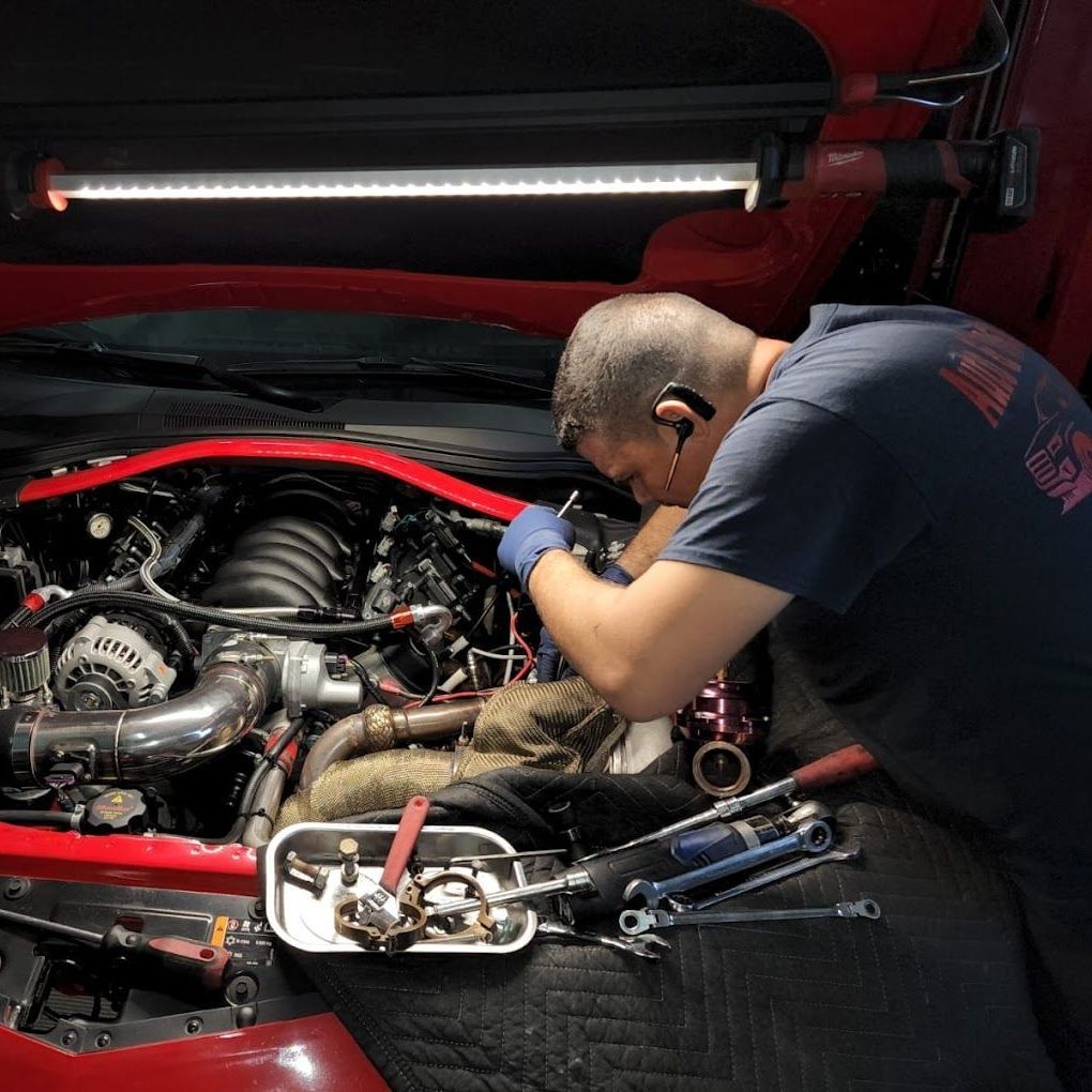 Mechanic working on a red car engine, illuminated by a bright overhead light | Auto & Truck Solutions