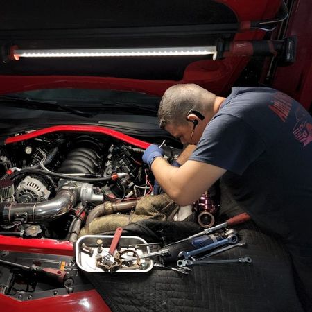Mechanic working on a red car engine, illuminated by a bright overhead light | Auto & Truck Solutions