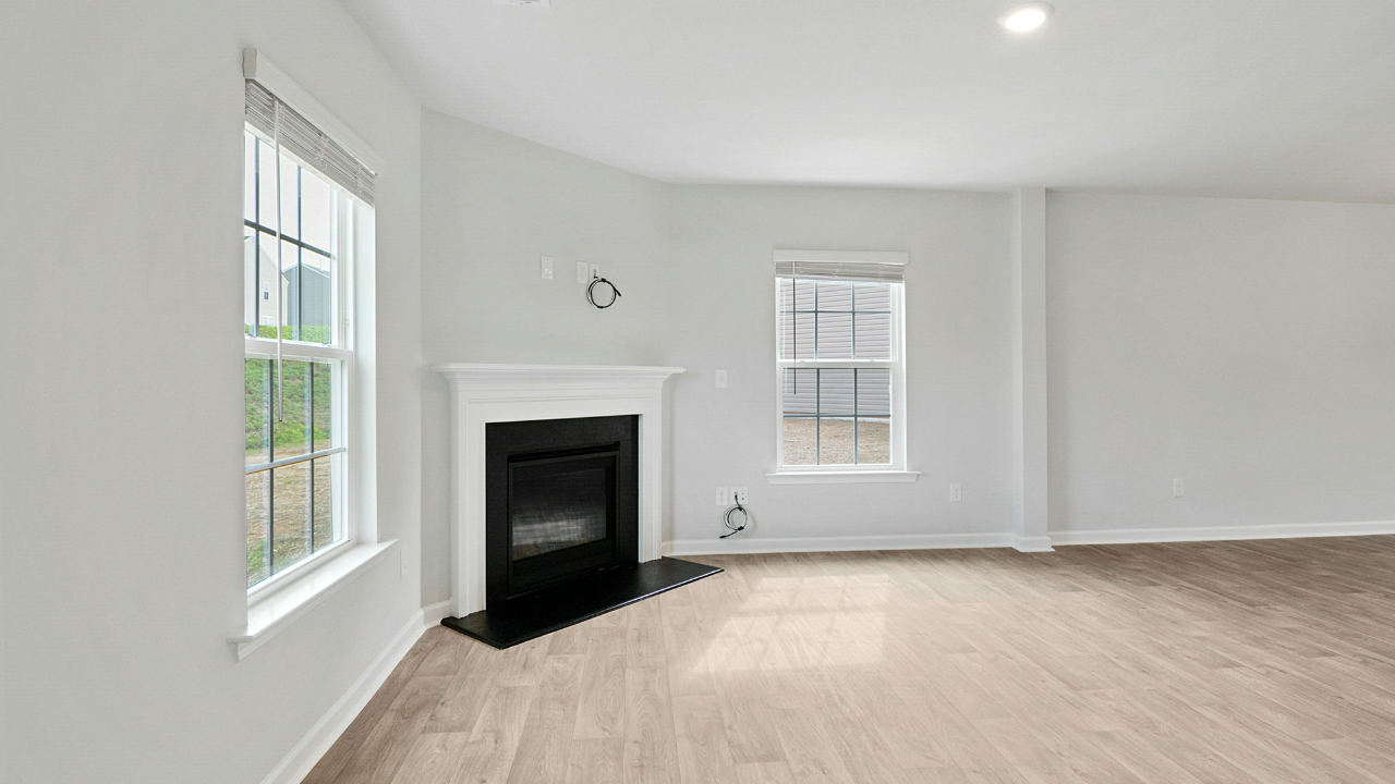 Living room with fireplace, windows, and light wooden floors. White walls and black fireplace.