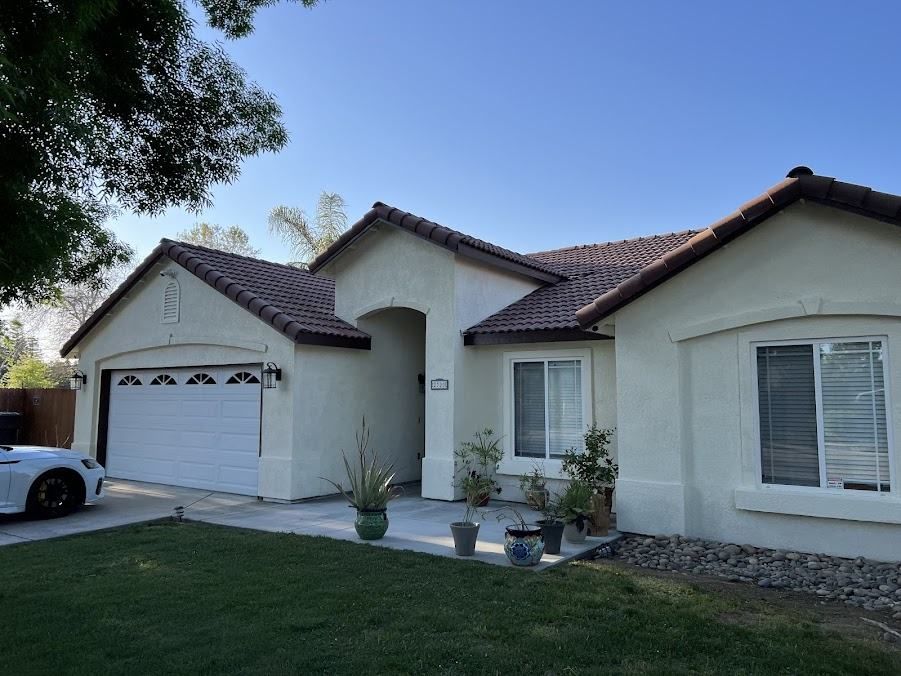 Beige house with a tiled roof, garage, and front yard with a car on the left.