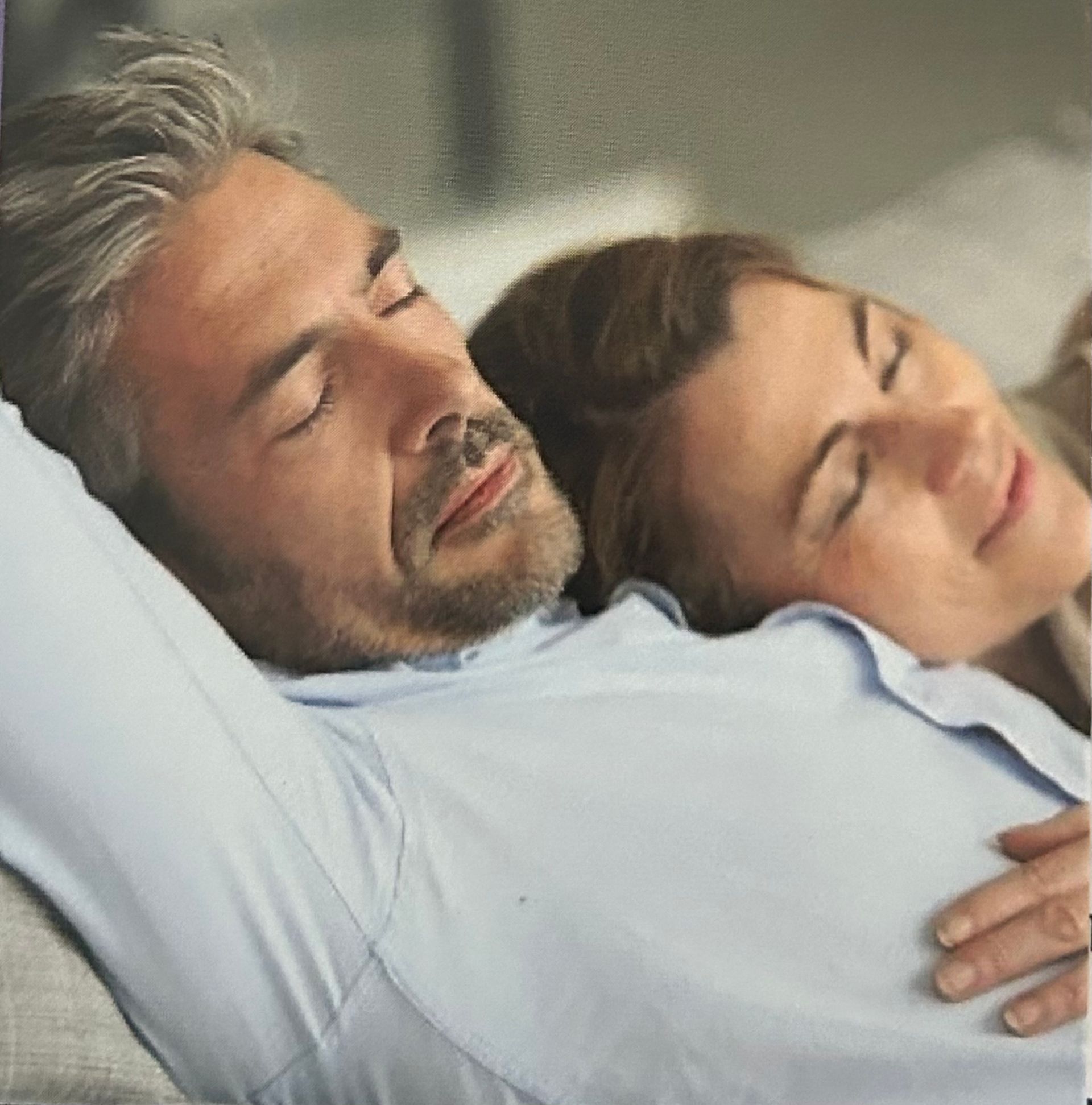 Couple asleep on a sofa, man in blue shirt, woman's head on his shoulder, both with closed eyes.