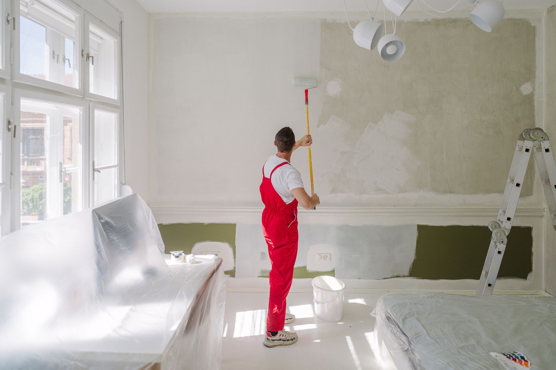 Photo of a professional house painter, in a red uniform, painting walls in the apartment. Photo of a professional house painter, in a red uniform, painting walls in the apartment.