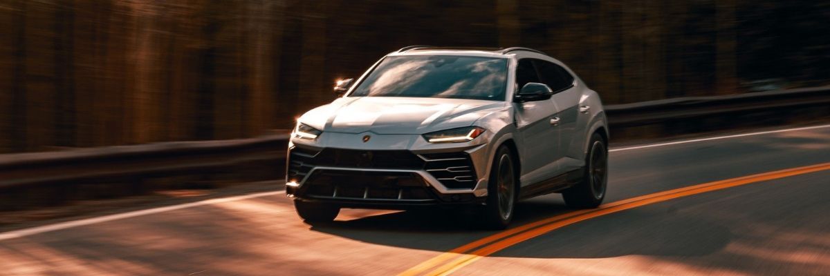 A window tinted white lamborghini urus is driving down a curvy road.