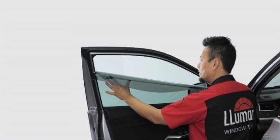 A man is applying window tinting to a car door window.