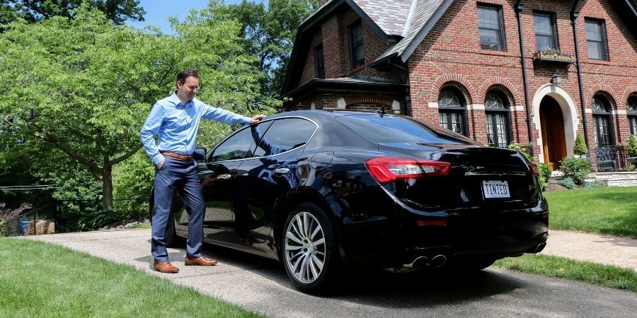 A man is standing next to a black car with FormulaOne tinted windows.