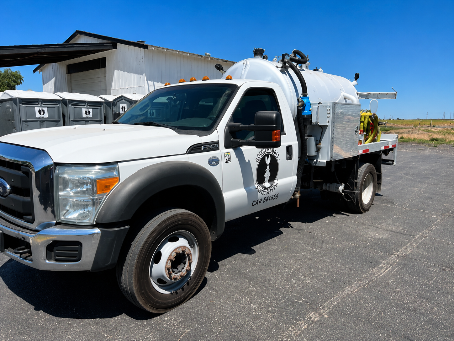White utility truck with tank parked on a sunny roadside near a building
