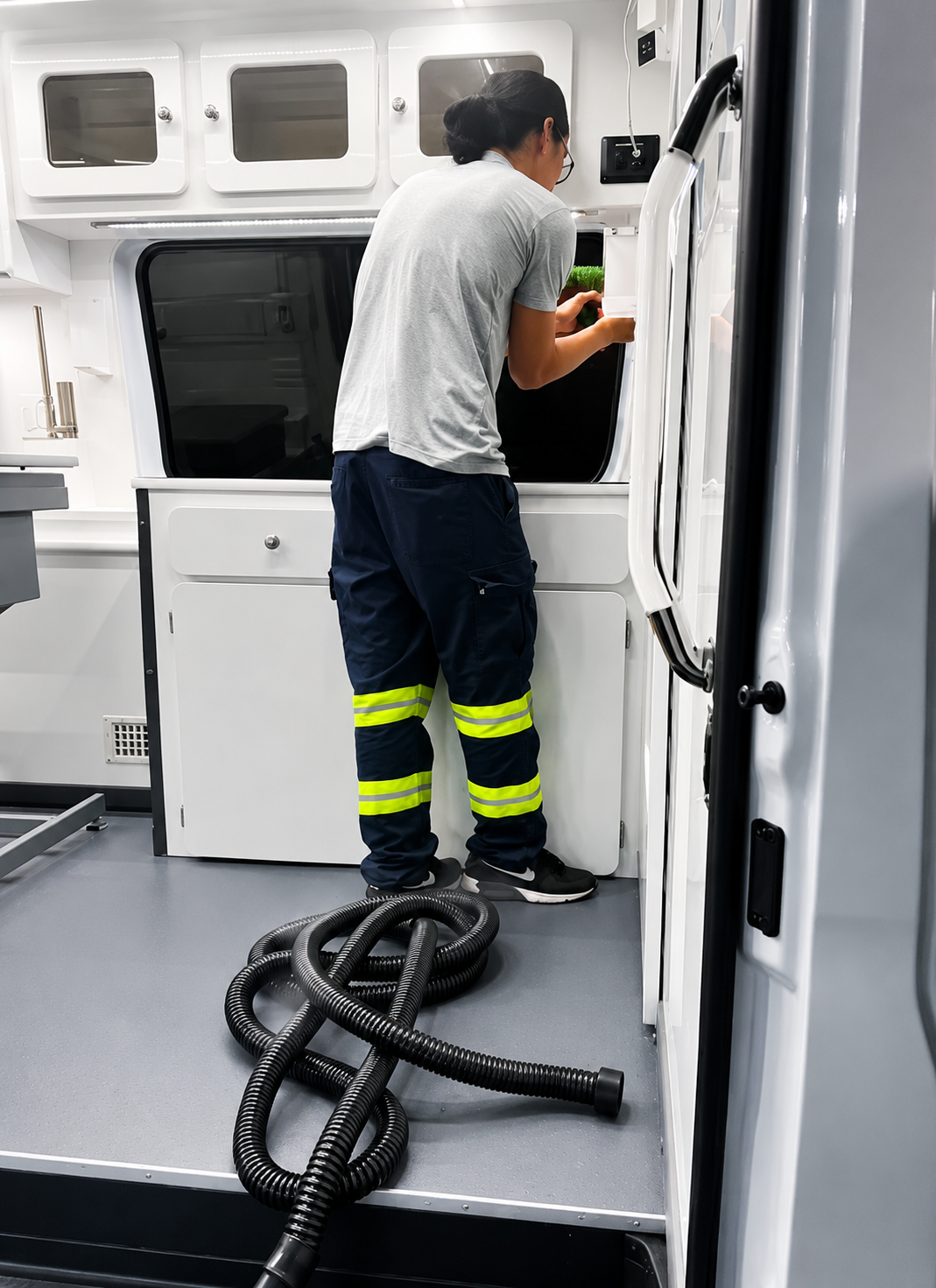 Technician inspecting control panel inside a white industrial machine, with black hoses on the floor.
