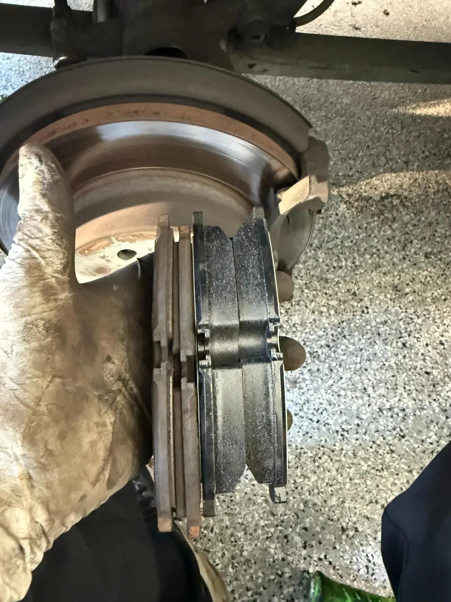 Close-up of a car brake rotor and caliper during wheel service, with a gloved hand nearby