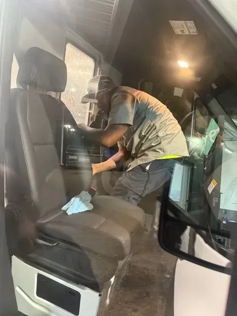 Person cleaning the interior of a vehicle, leaning into the front seat with a cloth and gloves.