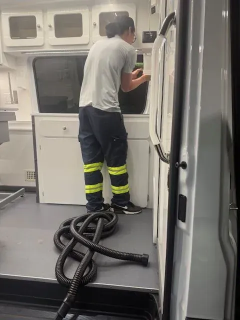 Worker standing in a white utility van, operating equipment with coiled hoses on the floor.
