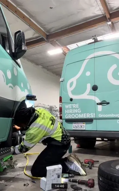 Worker fixing a mint-green van inside a garage, with another matching van nearby.